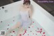 A woman sitting in a bathtub with rose petals on the floor.