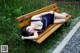 A woman laying on a wooden bench in the grass.