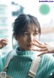 A woman in a green sweater is looking out a window.